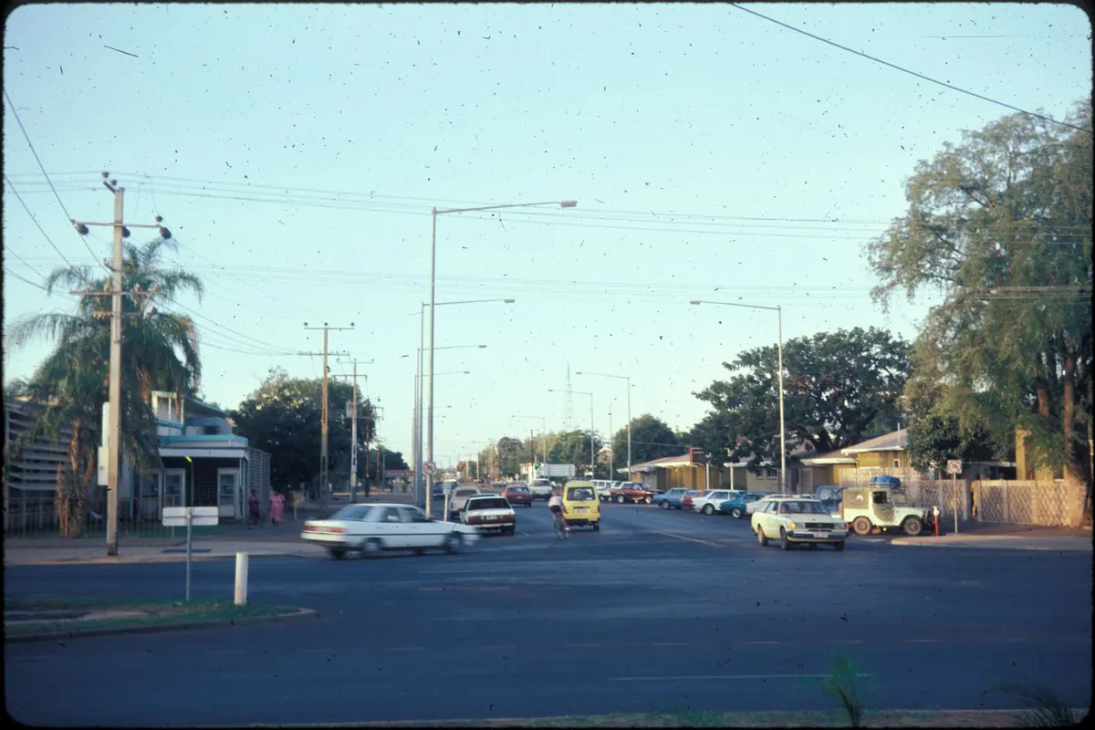 Una calle principal ancha con coches aparcados, postes de luz, una palmera y una oficina de correos a la izquierda, fotografiada en 1985